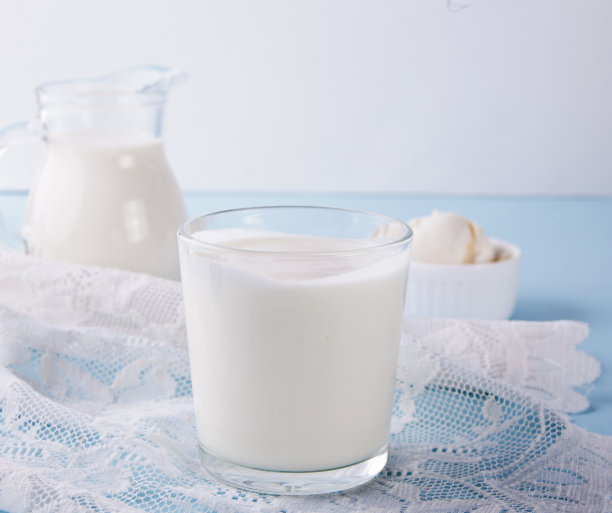 玻璃杯里的酸奶，桌上放着牛奶和奶油奶酪，还有白色的餐巾。图片下载