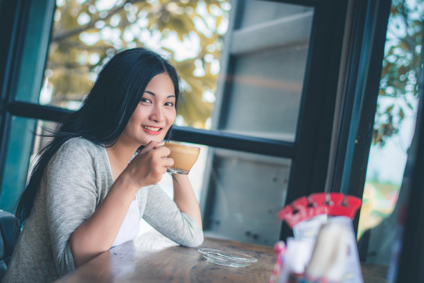 美丽迷人的年轻亚洲女人手里拿着一杯咖啡，坐在咖啡馆的沙发上在早上，复古的色调。图片下载