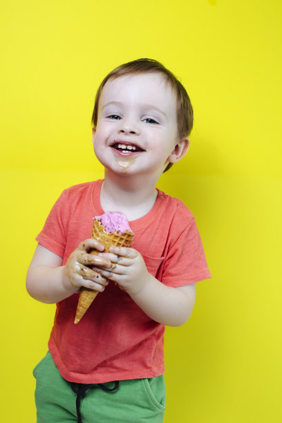 笑着吃着甜筒的男孩站在色彩鲜艳的墙的背景上，有夏天的心情和笑图片下载