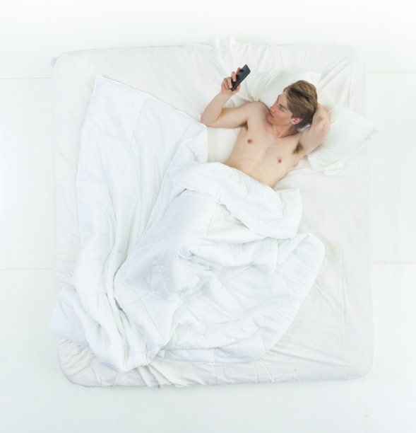 英俊的男人躺在床上，赤膊上阵，还在打电话图片下载