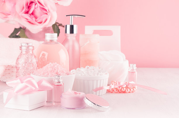 优雅的粉色皮肤和身体护理产品-霜，玫瑰油，液体肥皂，盐，棉毛巾和盒子-化妆品配件，浪漫的花在白色木质桌子上。图片下载