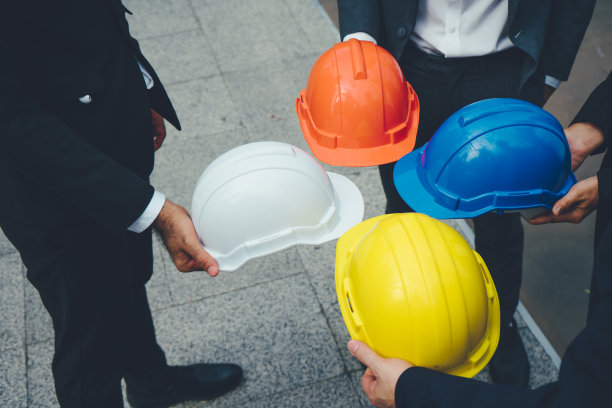 商人和工程师手持红、白、黄、蓝四色安全帽。团结协作的理念。图片下载
