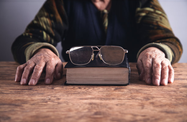 拿着书和眼镜的老年妇女的手。图片下载