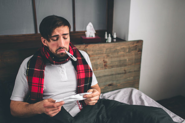 这是一个拿着手帕的年轻人的照片。病人躺在床上流鼻涕。人类研制出了治疗普通感冒的药。模特男性有高烧，头痛，偏头痛图片下载