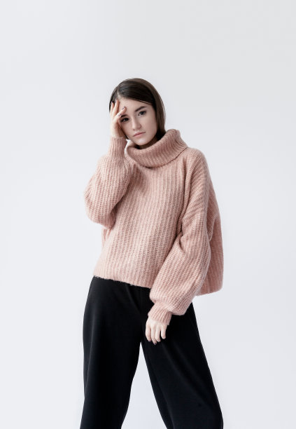 年轻漂亮的黑发女子穿着粉红色的宽松毛衣和黑色的裤子专业的自然妆容白色的背景图片下载