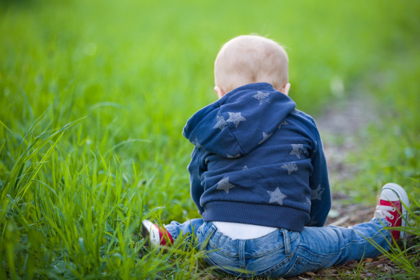 孩子坐在绿色的草地上。可爱的小孩坐在公园的绿草地上。孩子在户外。图片下载
