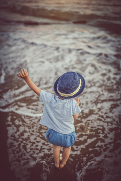 可爱的小男孩站在日落的海滩上图片下载