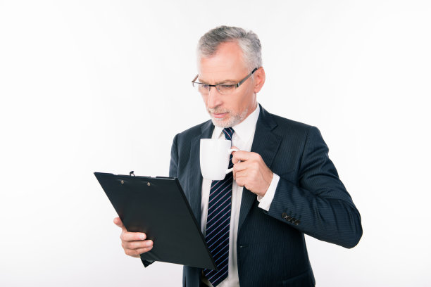 老自信的商人戴着眼镜，拿着杯子在文件夹里阅读信息图片下载