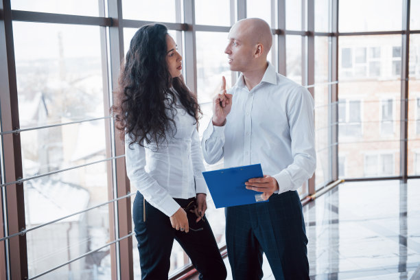 一名商人和一名女商人正在看车牌上的图表和一些纸质文件，这张照片位于城市办公室的一层高楼的背景上图片下载
