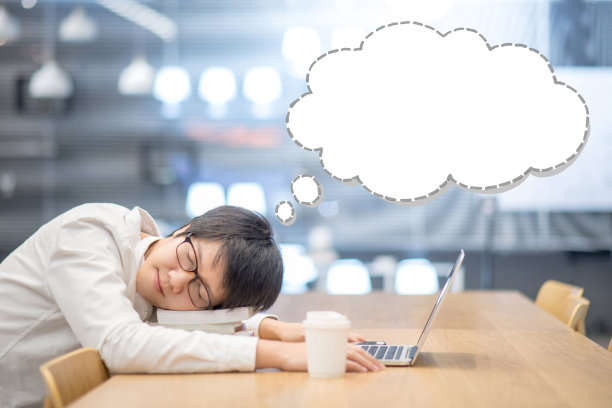 在大学图书馆的木桌上，一名年轻的亚洲男子大学生睡在一堆书上，头顶上空空如也的云图。学习间歇做个好梦。教育的概念图片下载