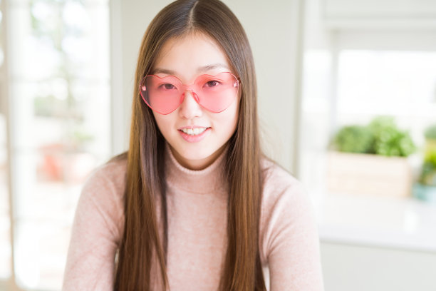 美丽的亚洲女人戴着粉红色的心型眼镜轻松与严肃的表情在脸上。简单自然的双臂交叉素材图片