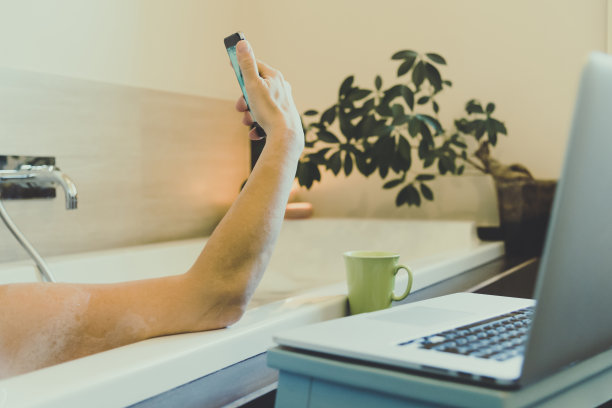 女人在浴缸的水里放松，女孩沉浸在沐浴放松的烛光气氛中放松。在家里工作的女孩在浴室里用笔记本电脑和智能手机。使用wifi技术在任何地方工作图片下载