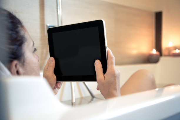 女人在浴缸的水里放松，女孩沉浸在沐浴放松的烛光气氛中放松。一个在家工作的女孩，浴室里有无线垫。使用现代wifi技术在任何地方工作图片下载