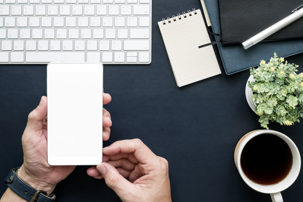 这张照片拍摄的是在办公室工作时用智能手机的人，俯视图的办公桌和办公用品。图片下载