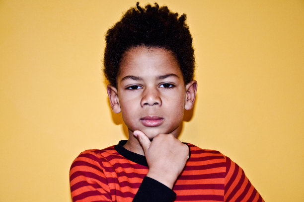 看起来很严肃的小男孩。黄色背景图片下载