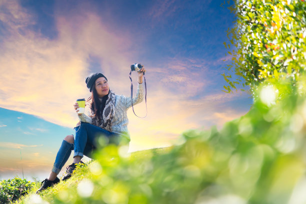 亚洲妇女在早晨拿着热茶杯喝着，拍着照片，坐在户外的茶园里，在阳光下享受着阳台上温暖的生活。生活方式的旅行。旅行和生活方式的概念。图片下载