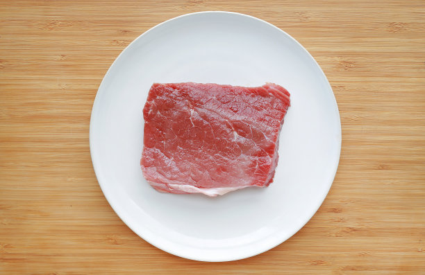 白盘子上的生牛肉，背景是木头。前视图。图片下载