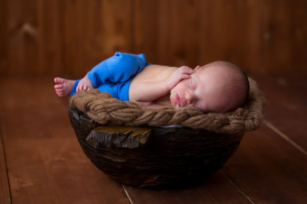 刚出生的男孩躺在一个圆木碗里，在粗糙的电缆地毯上，甜蜜地睡着了。图片下载