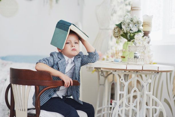 这张照片是一个勤奋的男孩，头上戴着一本书在做作业图片下载