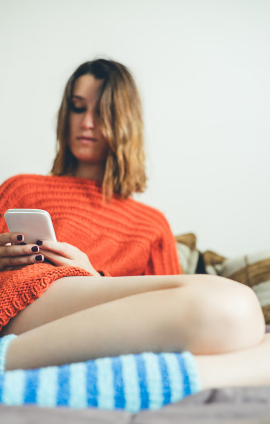 穿着彩色袜子的女人坐在床上玩手机。图片下载