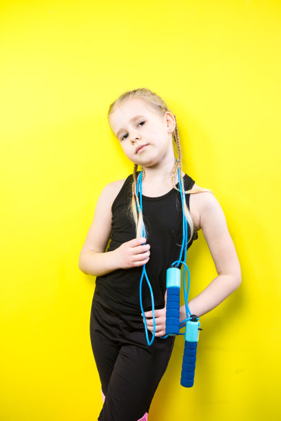 主题是体育与健康。美丽的白人小女孩与辫子摆黄色背景与微笑。小运动员手里拿着运动绳子。横幅广告空间，文字复制空间空白图片下载