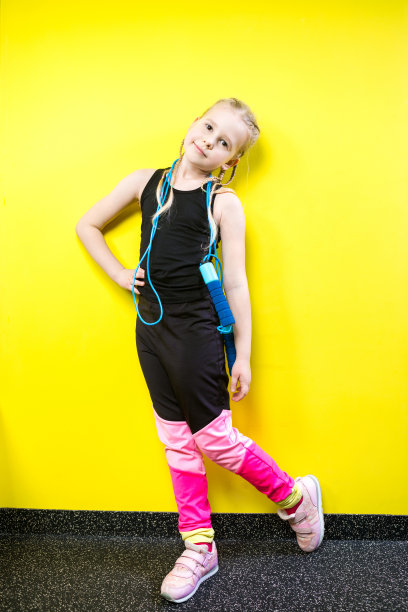 主题是体育与健康。美丽的白人小女孩与辫子摆黄色背景与微笑。小运动员手里拿着运动绳子。横幅广告空间，文字复制空间空白图片下载