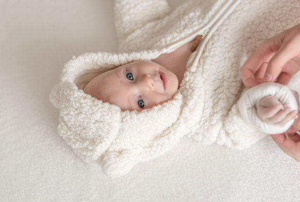 漂亮的小女孩穿着温暖的白色衣服躺在床上。图片下载