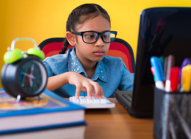 可爱的女孩戴着眼镜用笔记本电脑和计算器孤立在黄色的背景上。图片下载