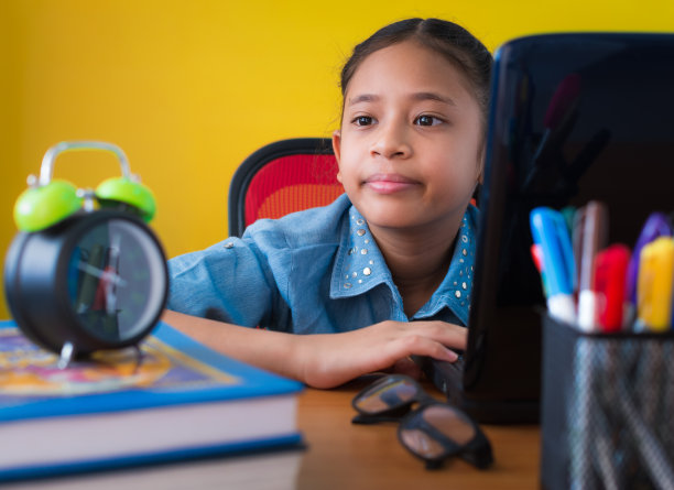 可爱的女孩使用笔记本电脑在工作桌上孤立的黄色背景。图片下载