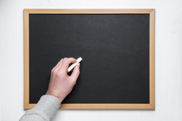 手拿粉笔在黑板上。男用粉笔在空黑板或黑板上写字。图片下载