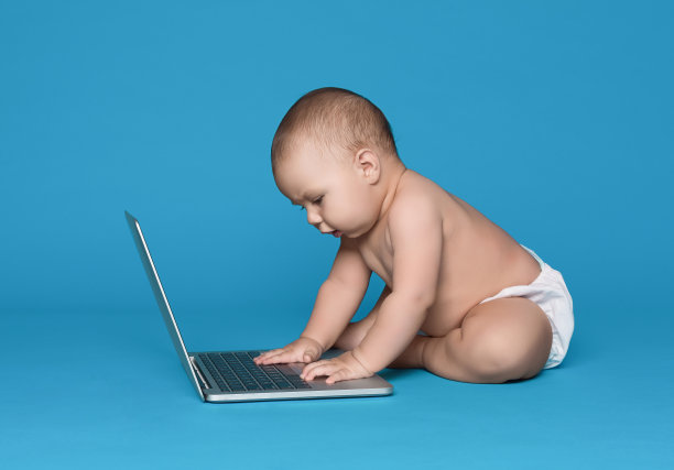 可爱的婴儿工作在笔记本电脑上的蓝色工作室背景图片下载