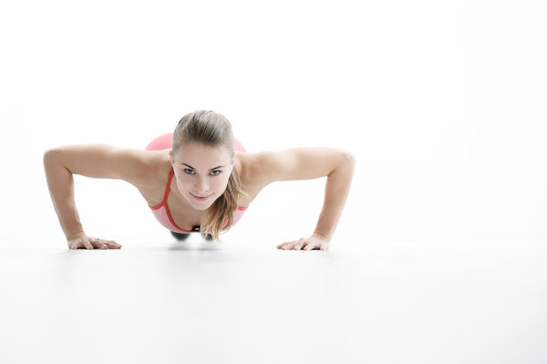 漂亮年轻的运动女人金发碧眼，穿着运动鞋和红色运动服在白色的地板上做俯卧撑。图片下载