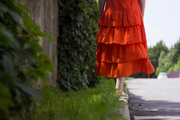 美丽的女人在橙色亚麻裙与褶边，夏季风格，时尚。那个女孩在路边图片下载