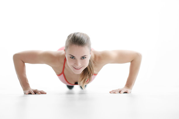 漂亮年轻的运动女人金发碧眼，穿着运动鞋和红色运动服在白色的地板上做俯卧撑。图片下载