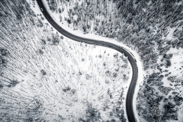 弯曲多风的道路在白雪覆盖的森林，从上到下鸟瞰图黑色和白色图片下载