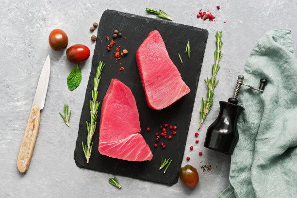 将新鲜的金枪鱼片放在带有香料的石盘上，灰色背景。平躺，俯视图。图片下载