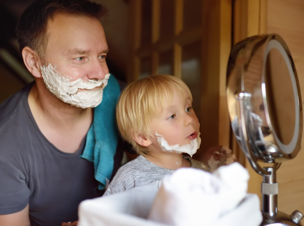 成熟的男人和小男孩在一起玩泡沫剃须。儿子学父亲的样。图片下载
