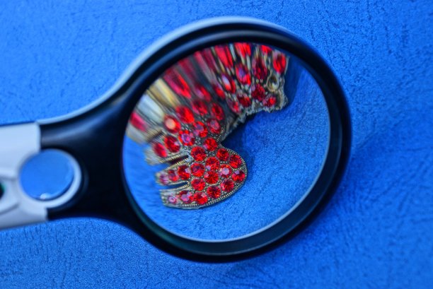 蓝色的桌子上放着圆形放大镜和金色的小红宝石图片下载