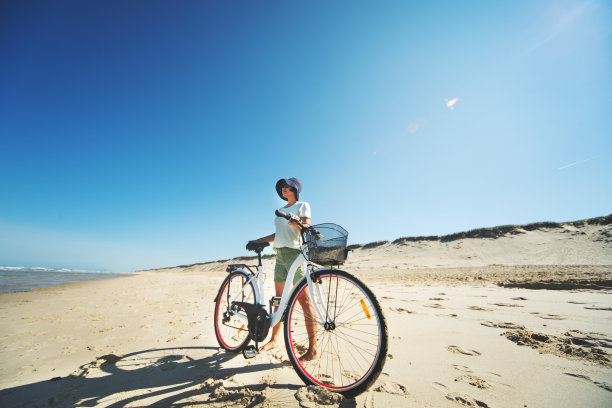 年轻的成年女子骑着自行车在海滩上图片下载