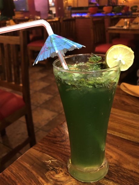 维珍莫吉托不含酒精的鸡尾酒在高球杯与橙色装饰和稻草，印度酒吧背景照片图片下载