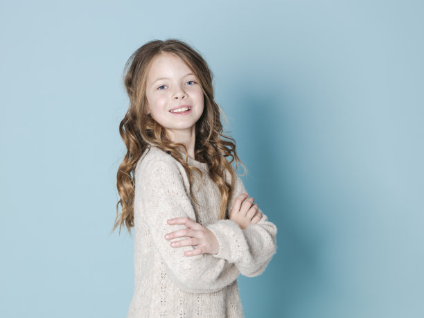 漂亮的，9岁小女孩与棕色羊毛衫在蓝色背景前摆姿势图片下载