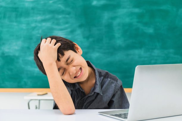 亚洲困惑的学校男孩使用笔记本电脑的黑板背景与疲劳和紧张的脸。幼儿创新教育的学生理念。图片下载