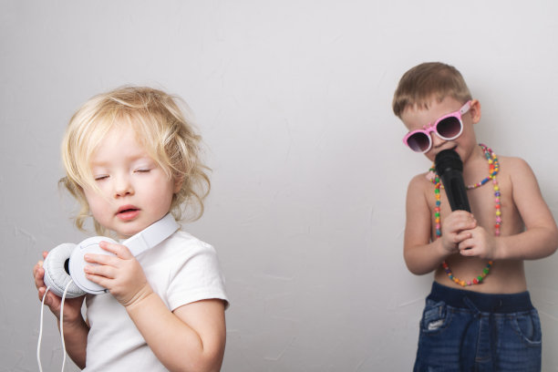 一个戴着墨镜的男孩对着麦克风为一个女孩唱歌。戴耳机的女孩闭上了眼睛。图片下载