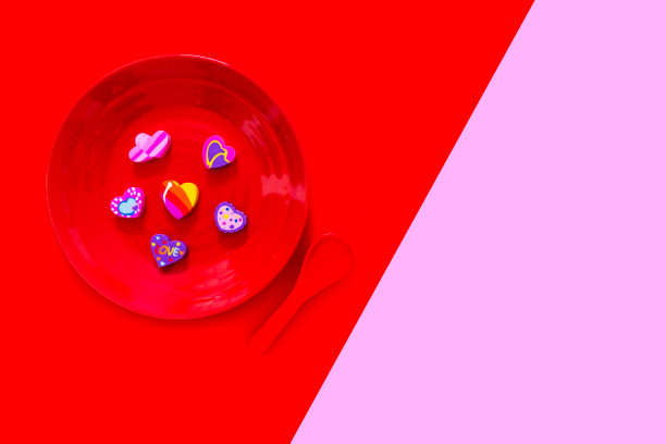 情人节是一个彩色的心在一个红色的盘子和勺子的爱情概念。心形的扁橡皮，带着浪漫。不同的橡胶心符号孤立在粉色和红色背景。图片下载