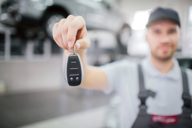 工人手里拿着的钥匙模糊的图片。他看着它，笑了笑。年轻人站在车库里。站台上有一辆车在他后面。图片下载