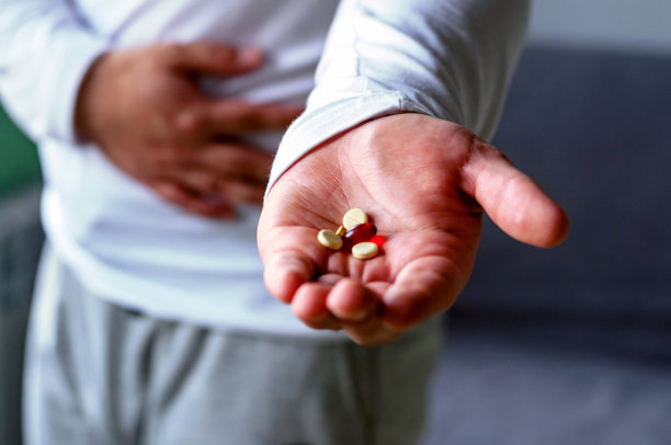 一个男人抓住他的肚子，用药片伸展他的手。健康、疾病、药物。有选择性的重点。图片下载