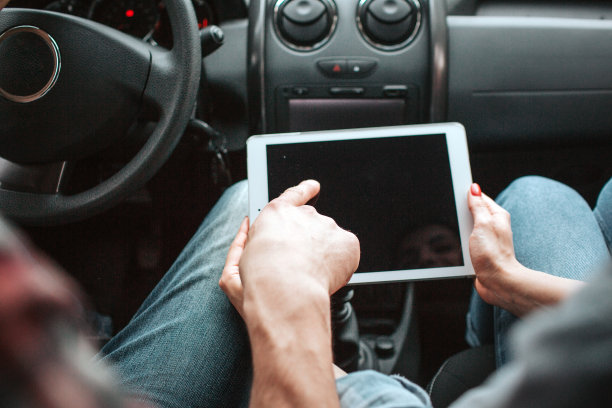 一张白色平板的图片。女孩的手握着它，而男人的手指指着黑色的屏幕。人们坐在车里。图片下载