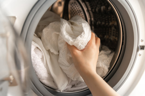 女人右手将白色衣服装进洗衣机的特写。图片下载