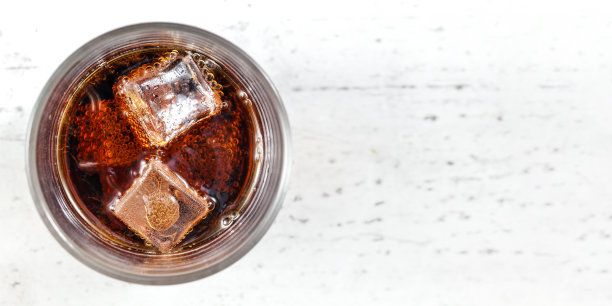 桌面视图，玻璃与可乐饮料和冰块在白板上。宽照片，文字右边的空间。图片下载