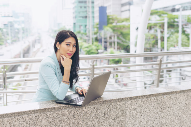美丽可爱的女孩微笑在商务女性服装使用笔记本电脑在城市城市背景-商业概念图片下载